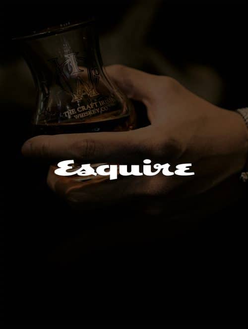 A hand holding a glass of luxury whiskey and esquire magazine