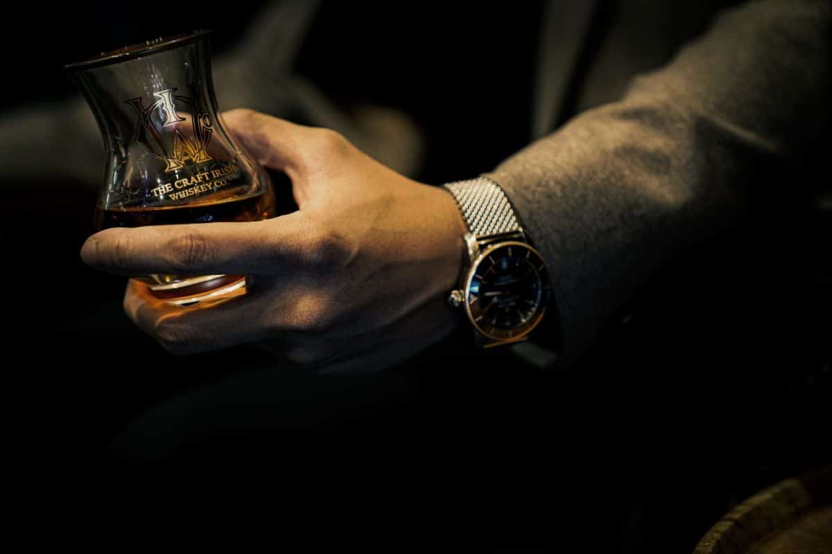 A person wearing a watch, holding a glass of rare whiskey